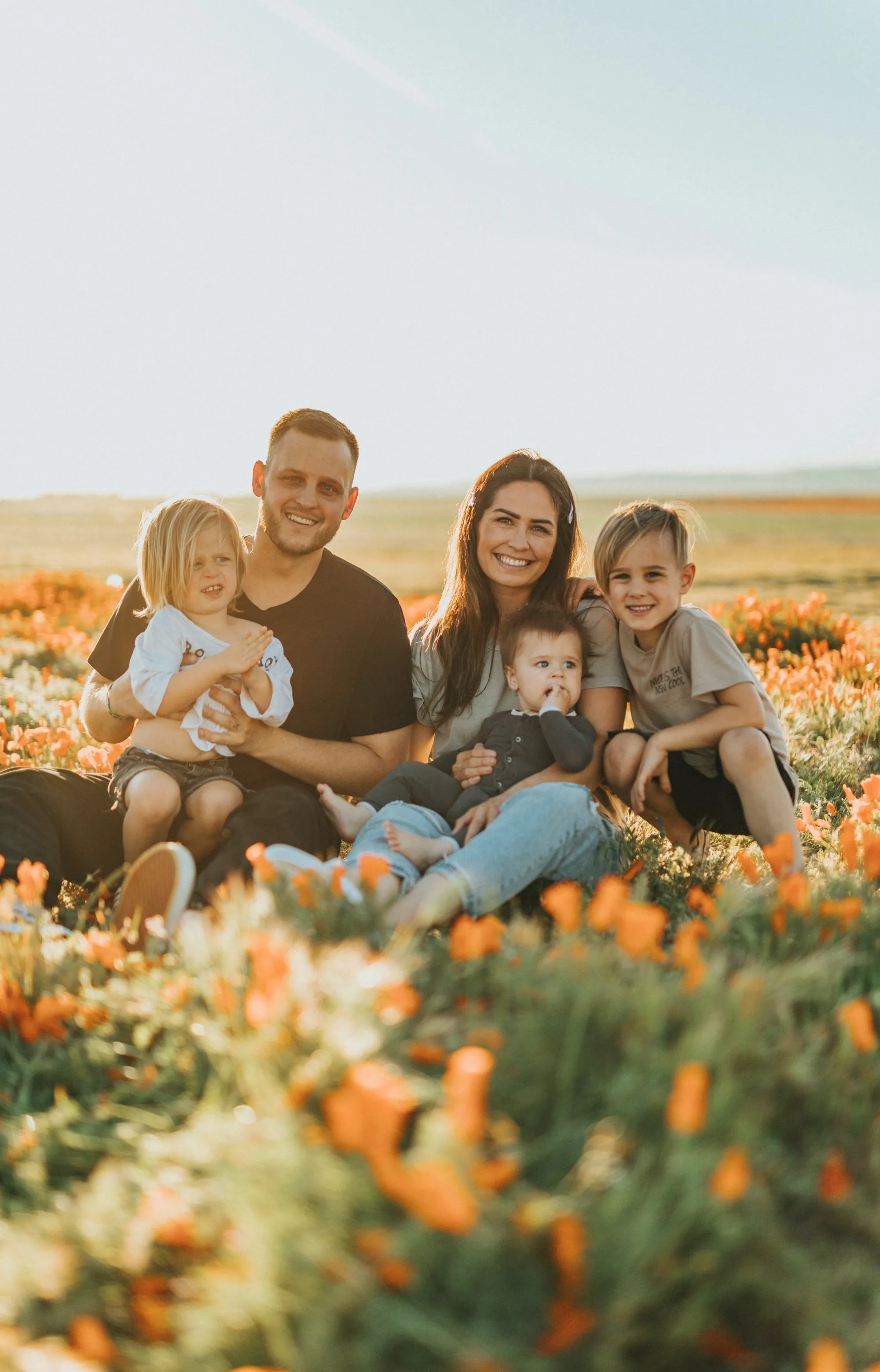 Parents and three young children sitting together in a field of wildflowers