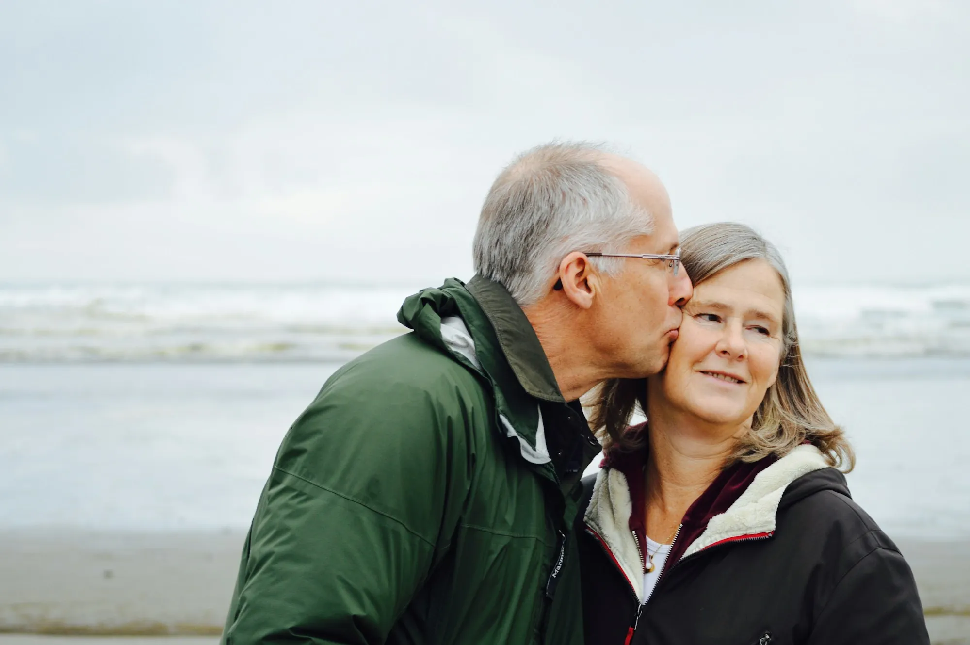Older man kissing his wife's cheek at the beach